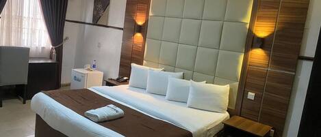 A hotel room with a large bed, a bedside table, a nightstand, a desk, and a chair.