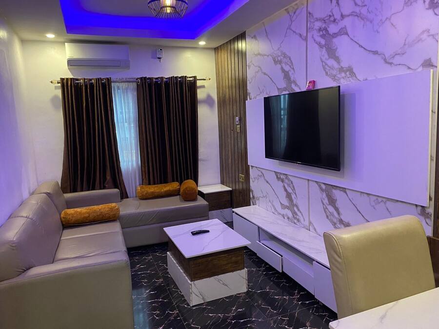 Una sala de estar moderna con un conjunto de sofá, una mesa de centro, un televisor montado en la pared y paredes con diseño de mármol.