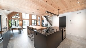 A modern kitchen with a central island, a dining area with a wooden table, and a staircase leading to an upper level. - Le Mitik Kanata Tremblant (224) (Amherst)