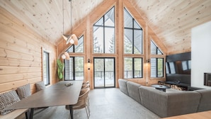 A spacious room with a wooden interior, a large dining table, a sofa, and a TV. - Le Mitik Kanata Tremblant (224) (Amherst)