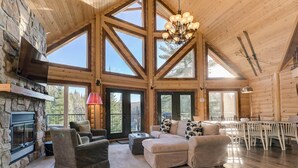 A spacious log cabin interior with a stone fireplace, large windows, and a dining area. - Baycliff Kanata Tremblant (257) (Amherst)