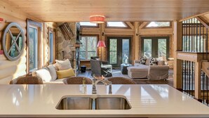 A log cabin interior with a central kitchen island, stone walls, and a cozy seating area with wicker furniture. - Baycliff Kanata Tremblant (257) (Amherst)