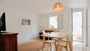 A modern living room with a wooden dining table, chairs, a television on a wooden cabinet, a woven light fixture, a framed picture, and a large window with a view of the outside. - Mundet 4 Dalt Terrassa. CostaBravaSi - At the sea (Sant Antoni de Calonge)