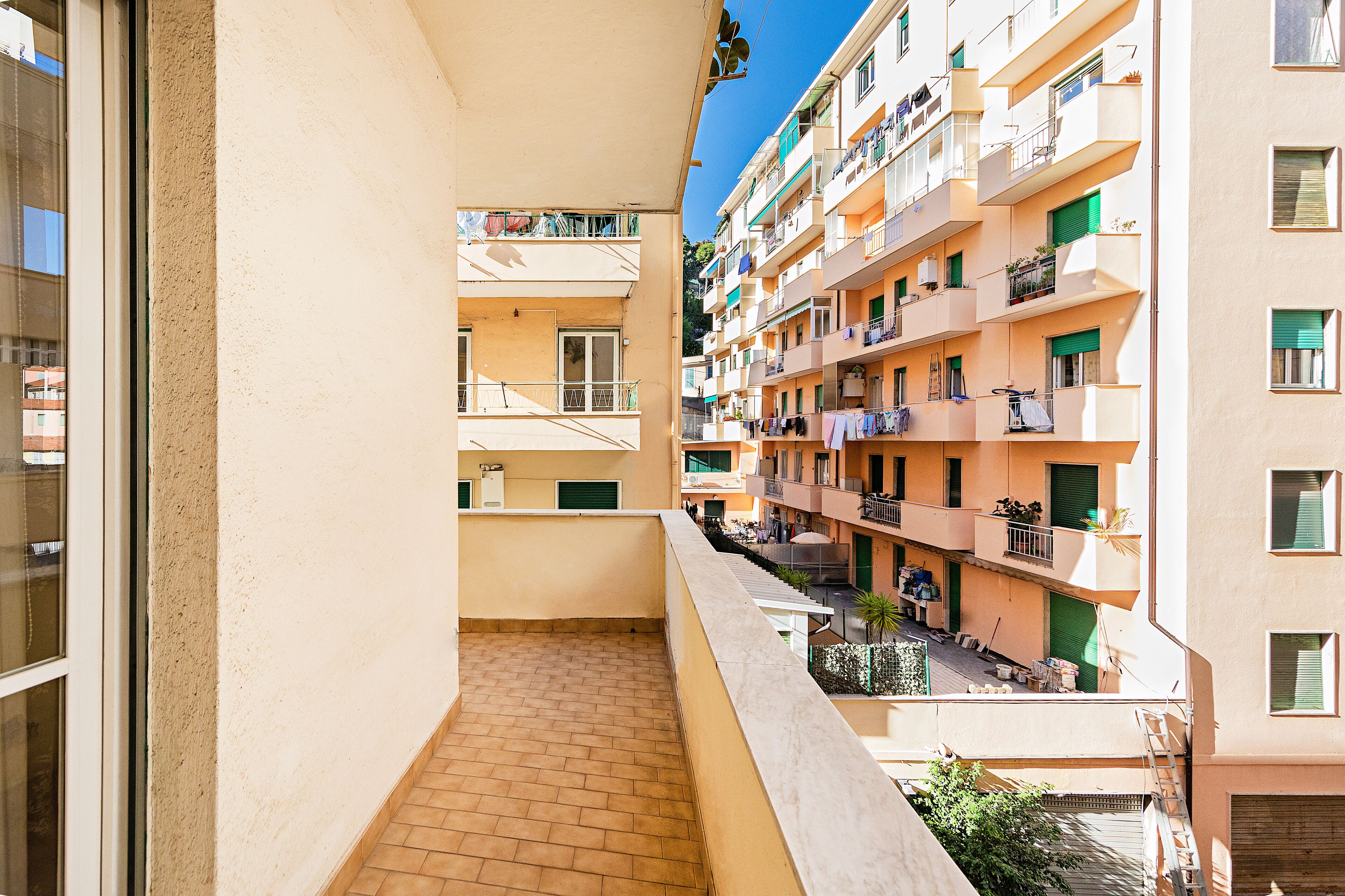 Un balcón estrecho con suelo de baldosas, con vistas a un edificio residencial de varios pisos con balcones y ventanas.