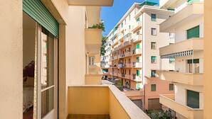 Ein schmaler Balkon mit Blick auf angrenzende Gebäude, eine Tür, die zu einem Raum führt, und ein kleiner Außenbereich mit einer Pflanze.
