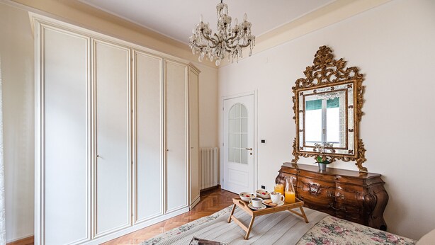 Ein Schlafzimmer mit großem Kleiderschrank, Schminktisch mit Spiegel, Frühstücksbrettchen und einem Bett mit floralem Überwurf.