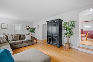 Una sala de estar con sofá, reposapiés y un mueble bajo de madera oscura.