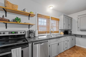 Una cocina moderna con electrodomésticos de acero inoxidable, estantes de madera y una ventana con persianas.