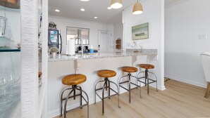 A modern kitchen with a central island, bar stools, pendant lighting, and a view of the living area. - "Beach Blessing" -Oceanfront Fun | Balcony (North Topsail Beach)