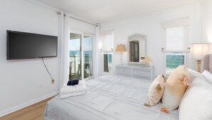 A bedroom with a large bed, a TV mounted on the wall, a dresser, and a view of the ocean through the window. - "Beach Blessing" -Oceanfront Fun | Balcony (North Topsail Beach)