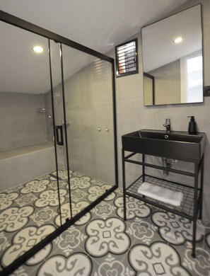 Une salle de bain moderne avec une douche à parois de verre, un lavabo noir avec un miroir au-dessus et des carreaux de sol à motifs.