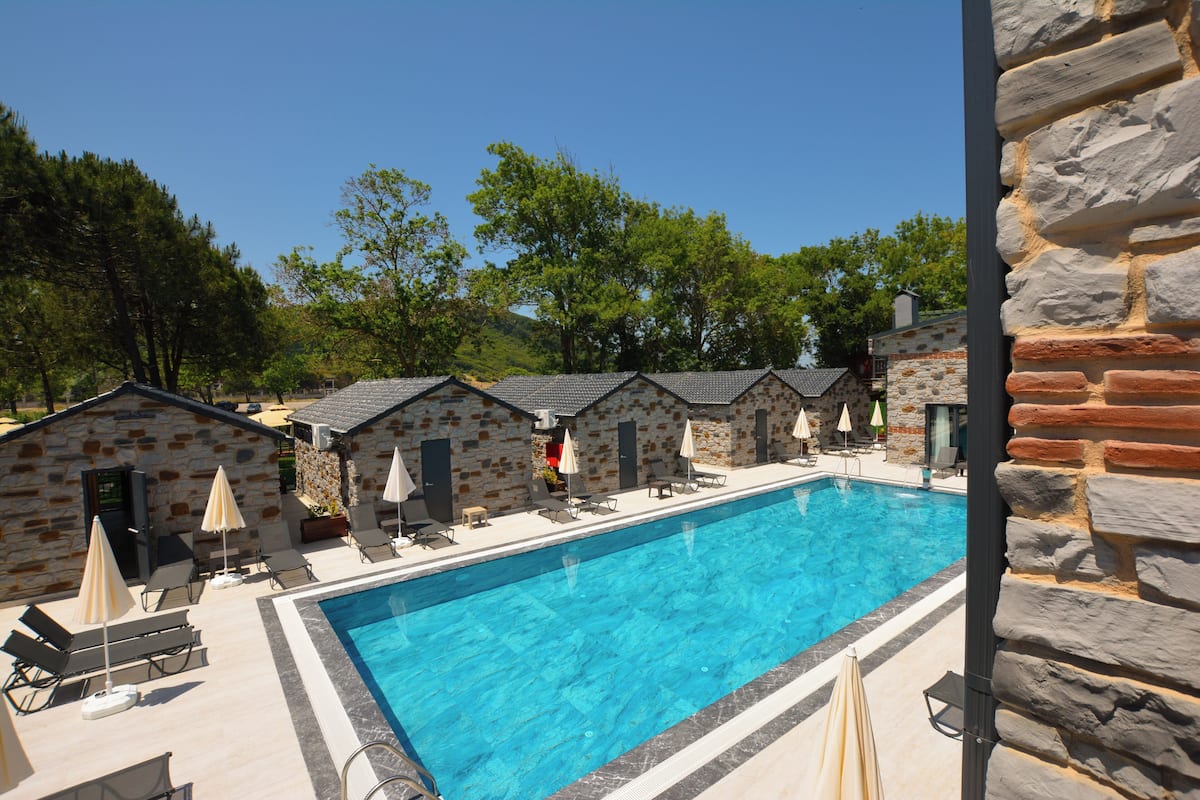 A swimming pool with lounge chairs and umbrellas, surrounded by stone buildings with doors and windows.
