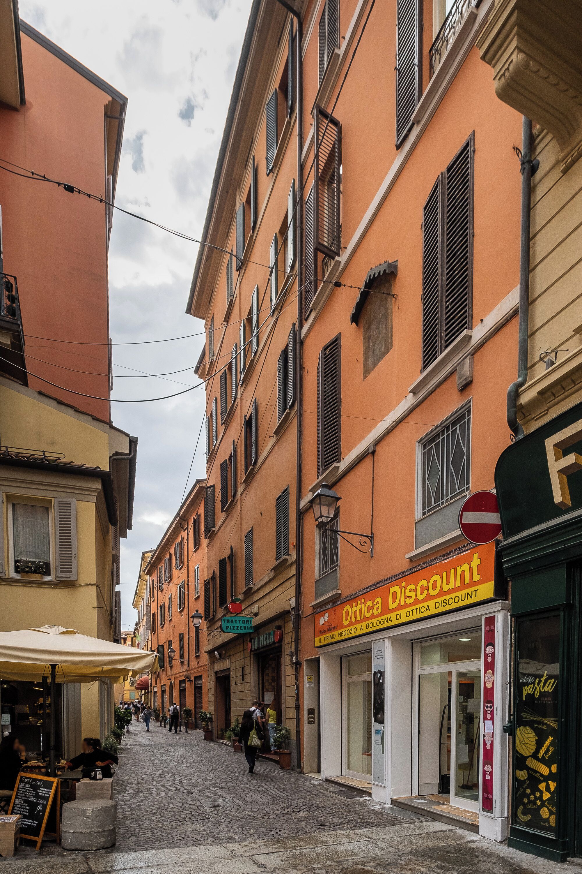 Una calle empedrada bordeada de edificios, incluyendo una tienda con un letrero que dice 'Ottica Discount'.