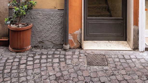 Un edificio con una puerta numerada (3), una planta en maceta y una escalera que lleva a un piso superior.