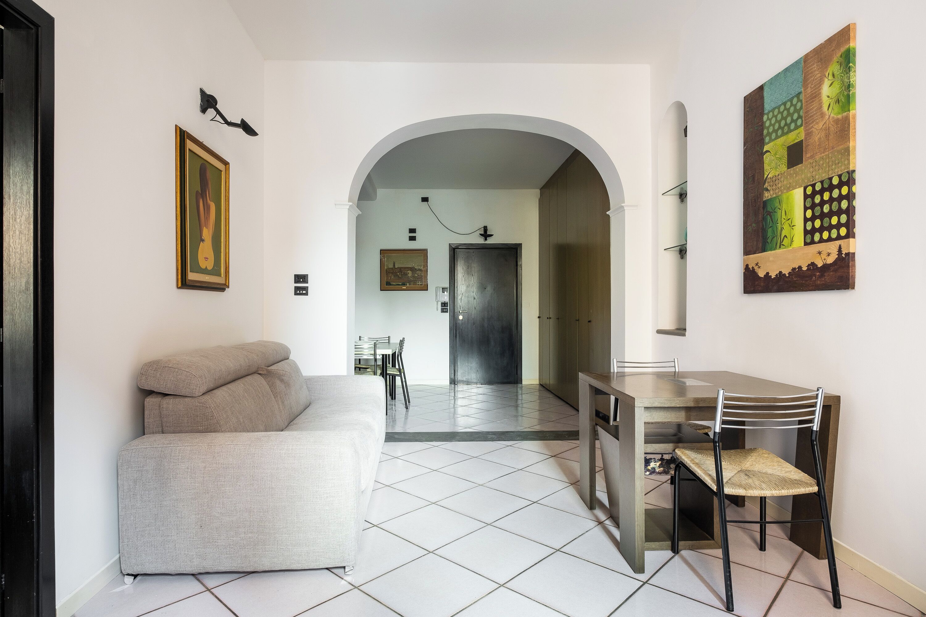 A modern interior with a sofa, dining table, and chairs, an archway leading to a hallway, and artwork on the walls.