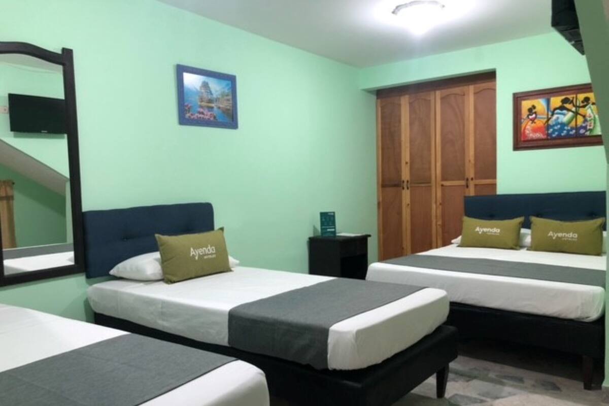 A room with two beds, each with a pillow labeled "Ayenda." There is a wooden wardrobe and a framed picture on the wall.