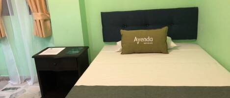 A hotel room with a bed, a nightstand, a pillow with the hotel's name, and a green wall.