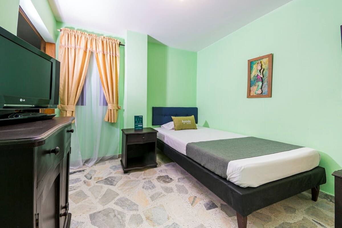 A bedroom with a bed, a nightstand, a TV, and a painting on the wall.