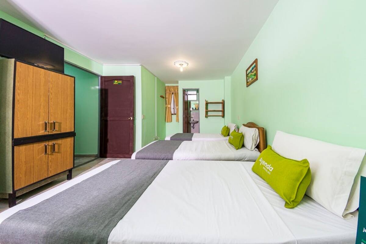 A hotel room with two beds, a wardrobe, and a door leading to another room.
