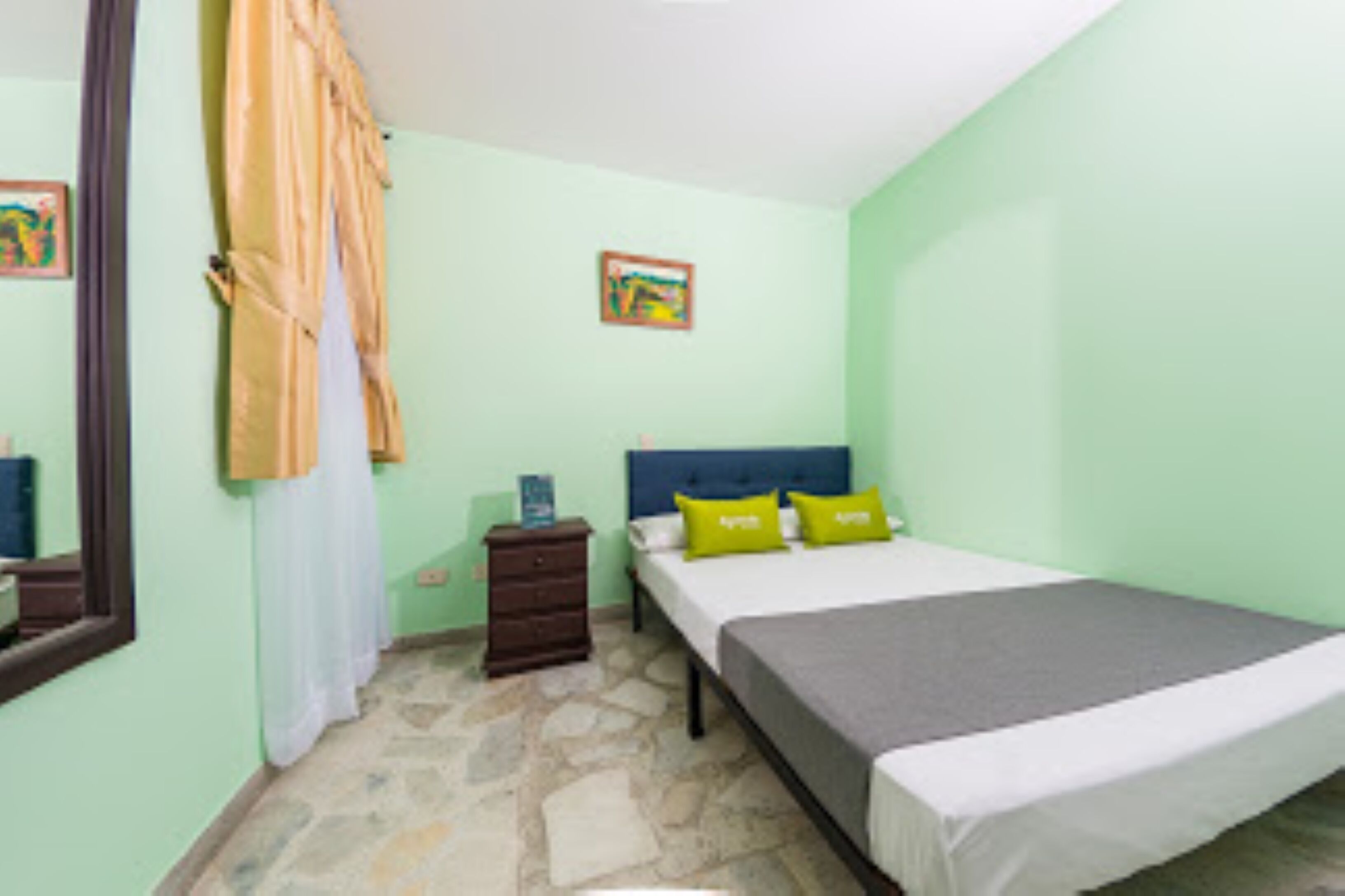 Un dormitorio con cama, mesita de noche, cómoda, espejo y un cuadro en la pared.