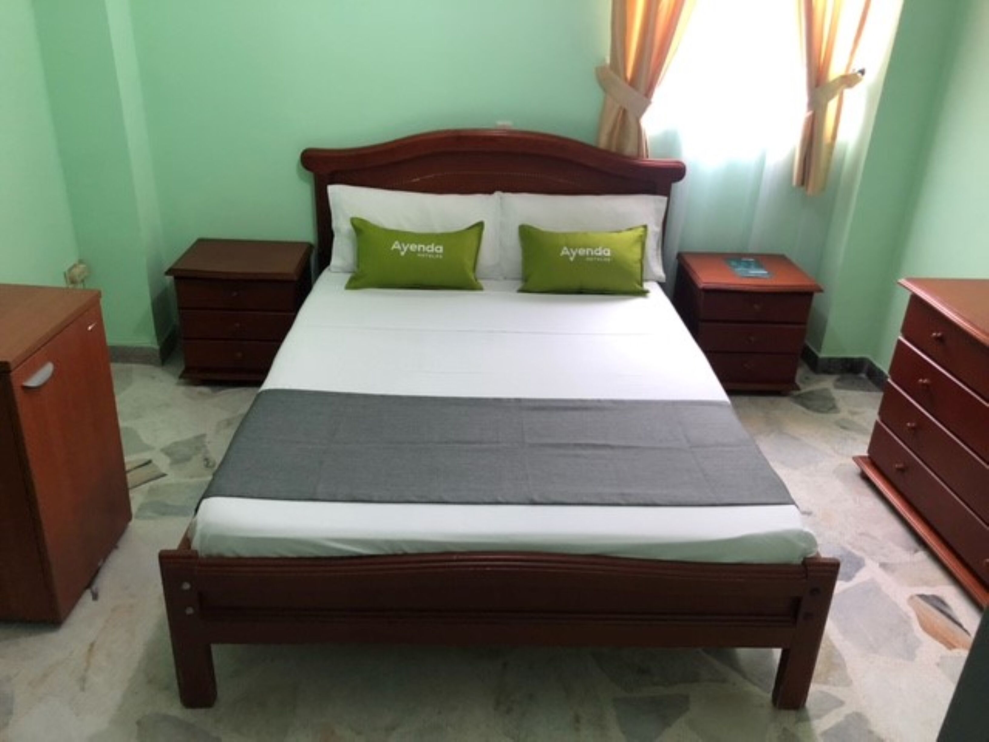A neatly arranged bedroom with a wooden bed, two nightstands, a dresser, and a green wall.