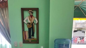 A room with a green wall, a wooden table with a water dispenser and a framed picture. - HOTEL EL BOSQUE ARMENIA (Armenia)