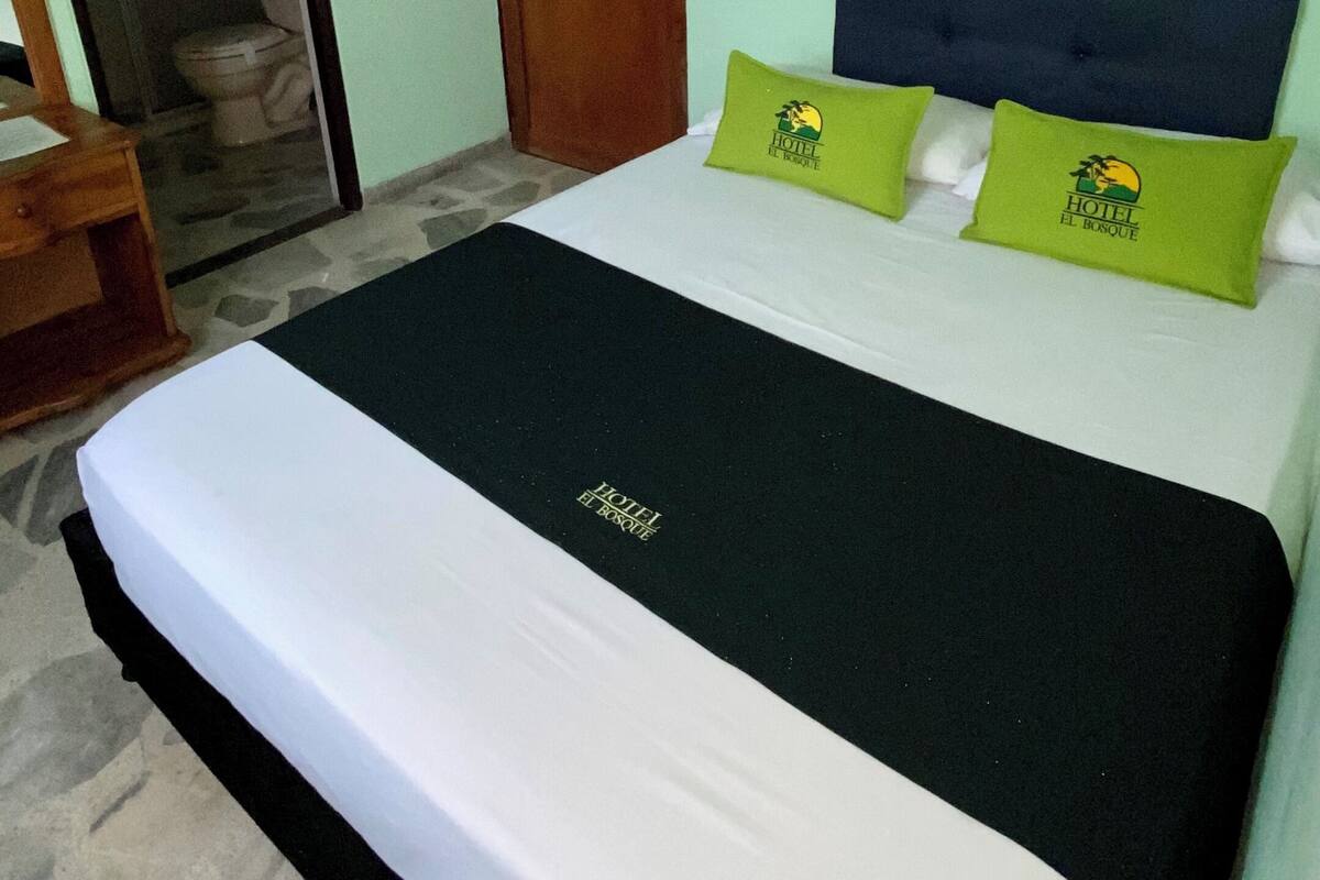 A hotel room with a bed, two pillows, a wooden door, and a bathroom visible through an open door.