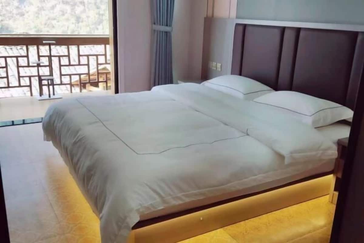 A neatly made bed with white linens, a wooden headboard, and a view of a balcony with a patterned railing.