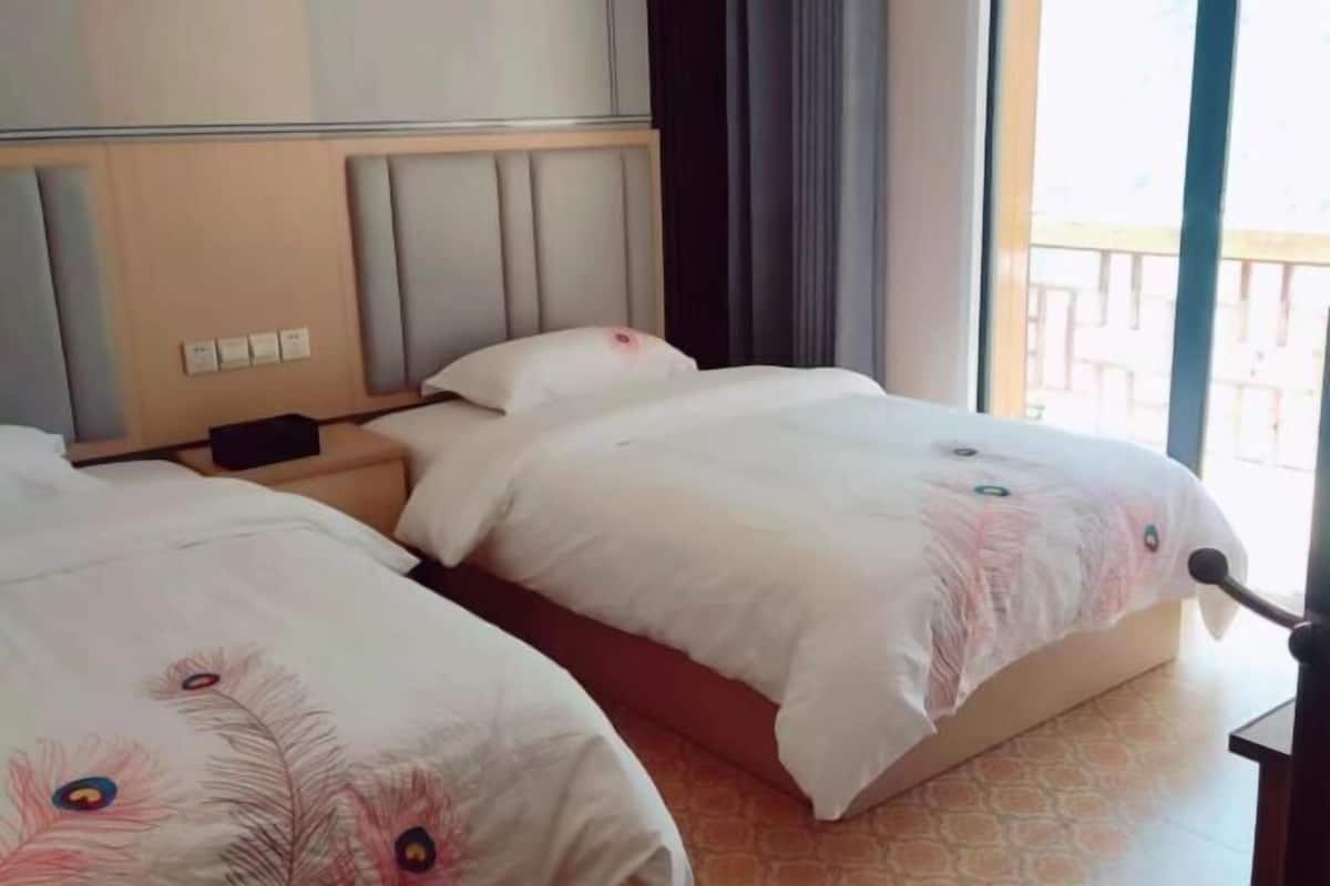 A hotel room with two beds, a headboard, a nightstand, and a window with a view.