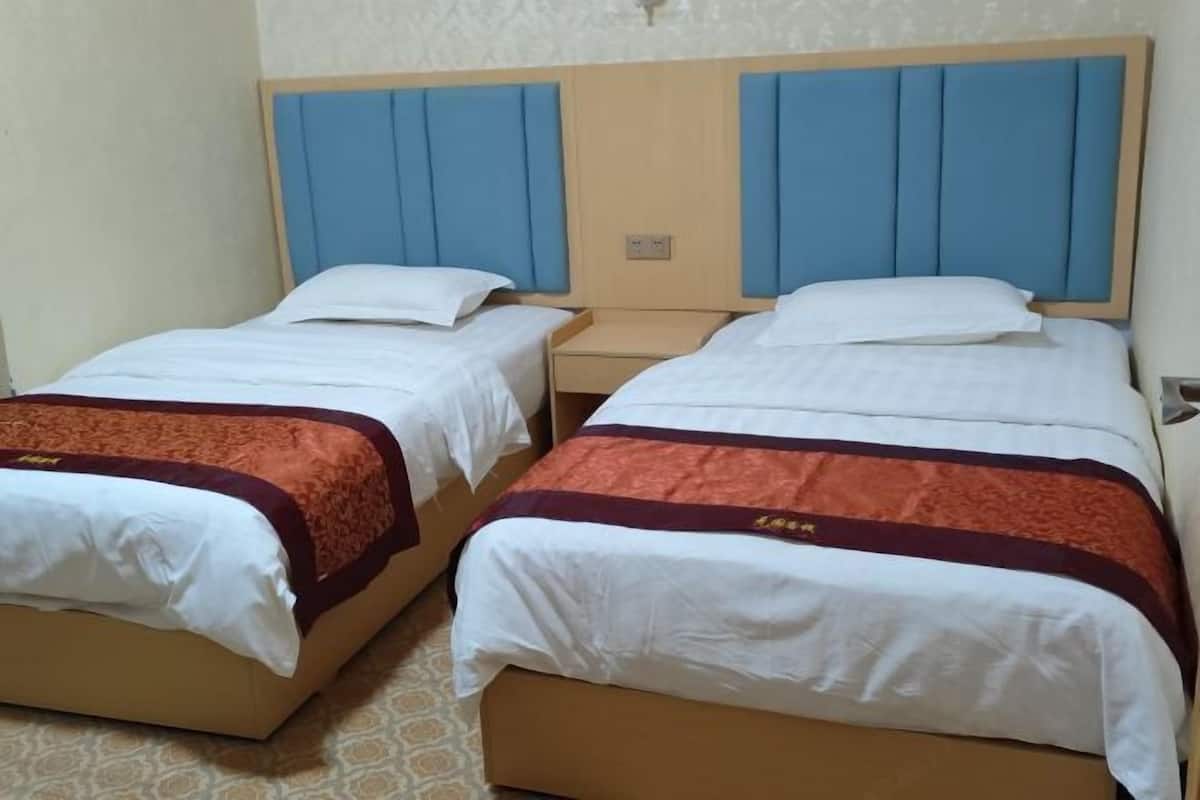 A hotel room with two single beds, each with a wooden headboard and blue panels.
