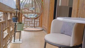 Un balcon en bois avec un fauteuil suspendu, un pot de fleurs et un fauteuil rembourré agrémenté d’un coussin à carreaux.