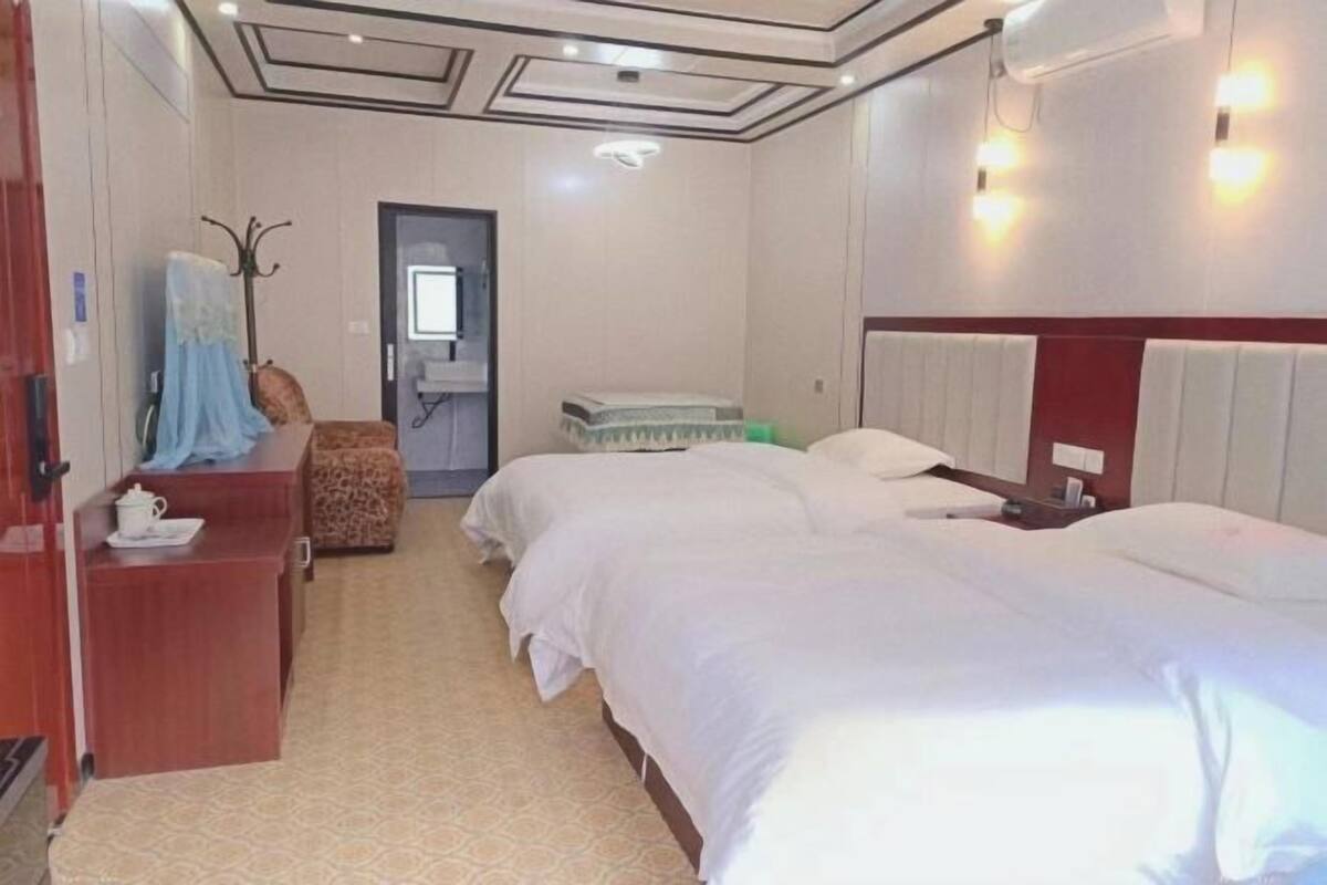 A hotel room with two beds, a wooden desk, a chair, and a small table with a cup.