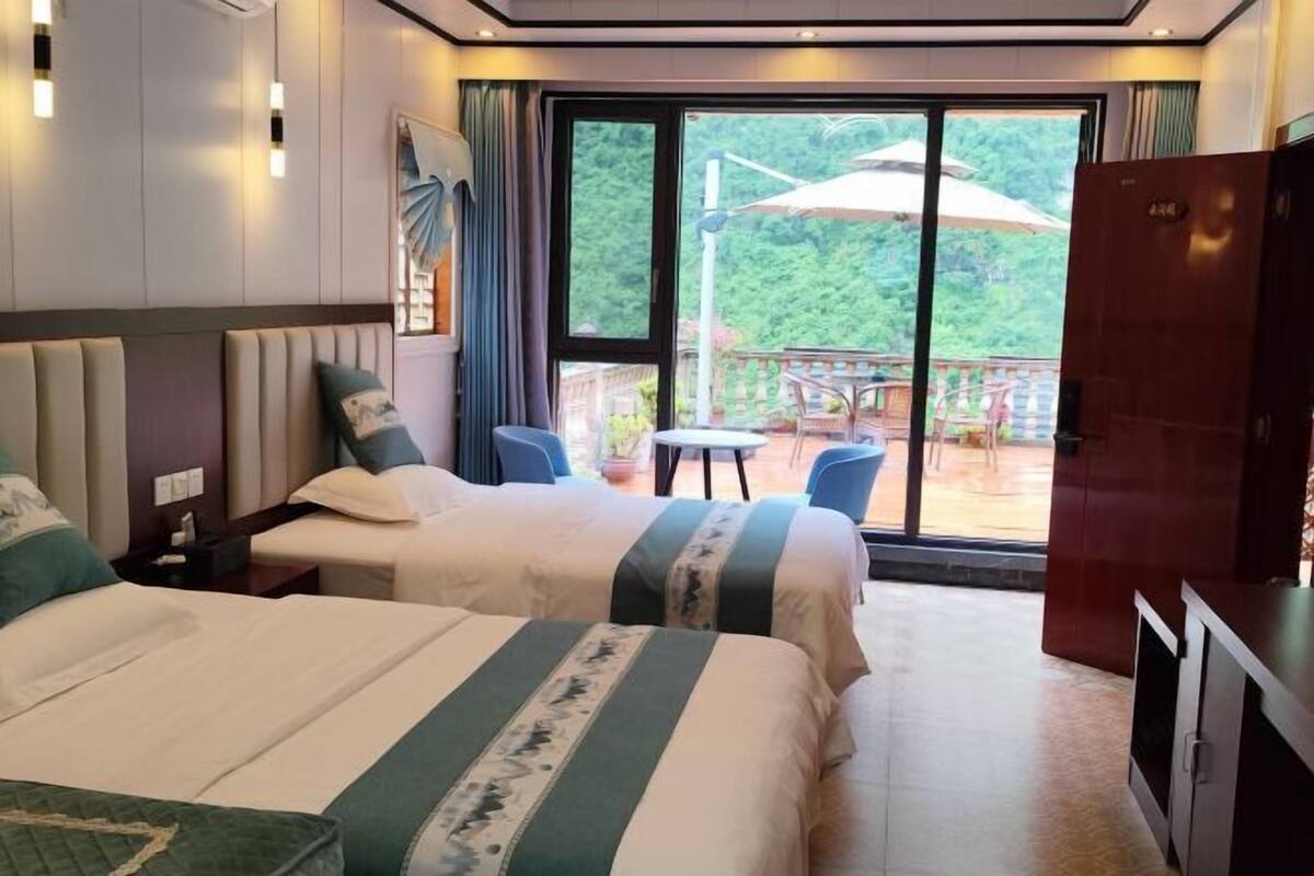 A hotel room with two beds, a view of the outdoors, a dining area, and a wardrobe.