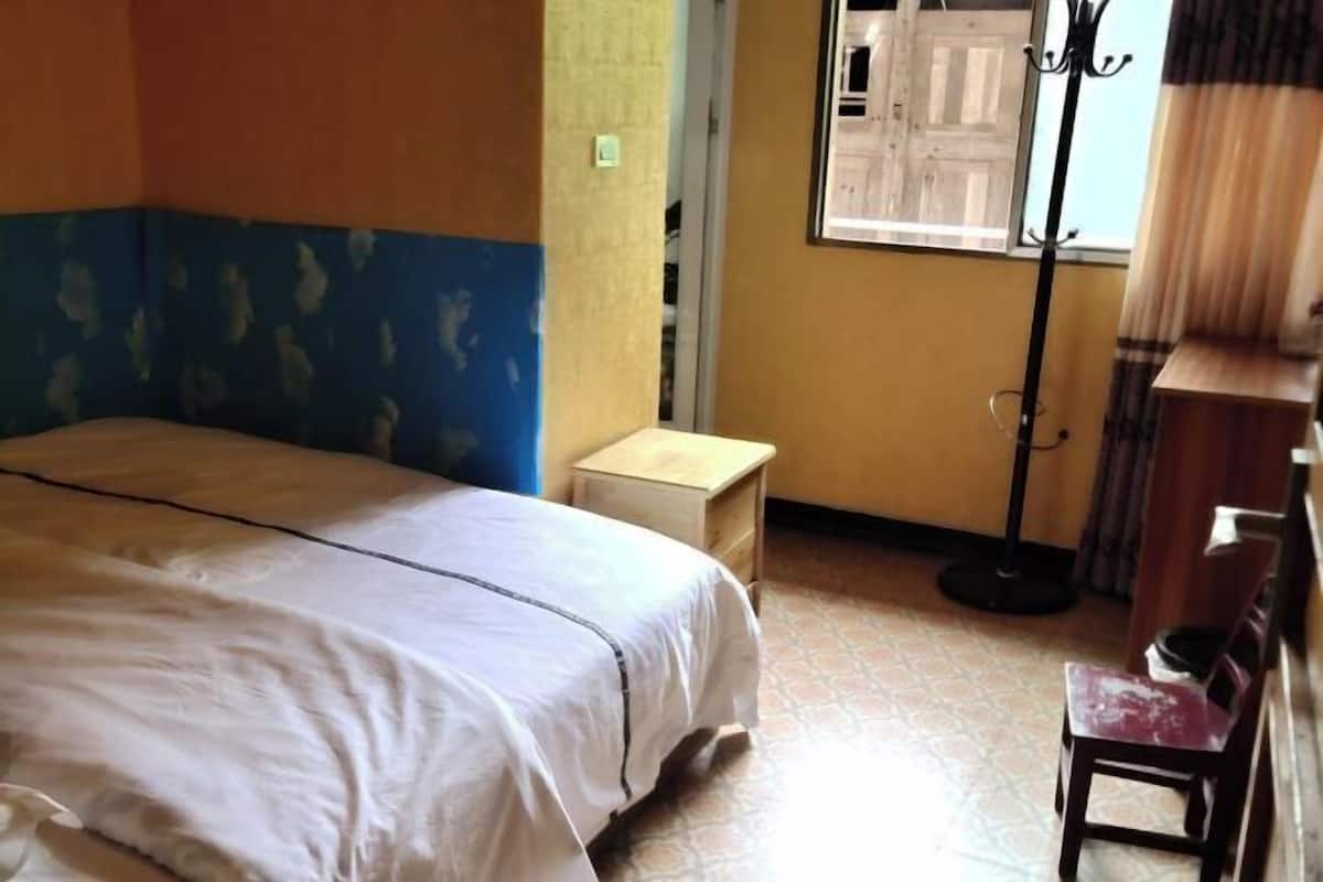 A room with a bed, a small wooden nightstand, a chair, and a floor lamp.
