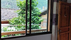 Une pièce dotée d’une grande fenêtre donnant sur une maison traditionnelle et une végétation luxuriante.