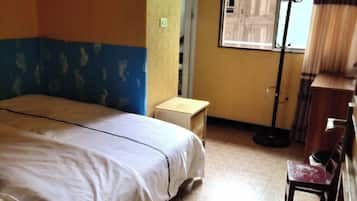 A room with a bed, a small wooden nightstand, a chair, and a floor lamp.