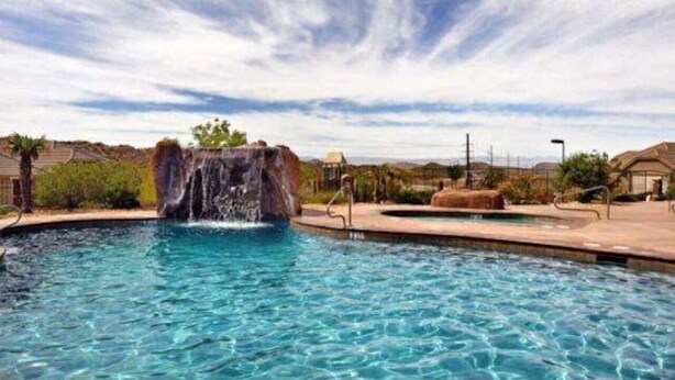 A swimming pool with a waterfall feature, surrounded by a landscaped area with a clear sky. - Get together at Zion`s Gate l & ll! (Washington)