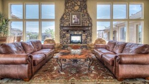 A spacious living room with leather sofas, a stone fireplace, and large windows offering a view of the surrounding area. - Get together at Zion`s Gate l & ll! (Washington)