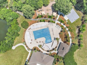 An aerial view of a residential area with a swimming pool, surrounding greenery, and a tennis court.