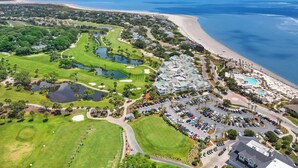 An aerial view of a coastal resort with a golf course, beachfront, and a parking area. - Seabrook Marsh Views | Amenity Card! | Pool Access (Seabrook Island)