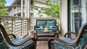 A balcony with wicker furniture, a glass table, and a view of a building with balconies. - Seabrook Marsh Views | Amenity Card! | Pool Access (Seabrook Island)