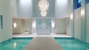 A modern hotel lobby with a reception desk, a large chandelier, and a pool area. - One Cable Beach (Nassau)