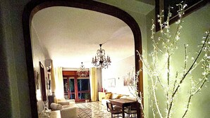 A hallway with a patterned floor leading to a living room with a chandelier, a dining area, and a potted plant.