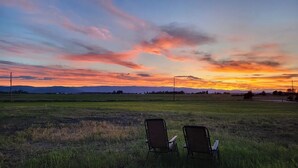 Deux chaises sont placées face à face, donnant sur un coucher de soleil au-dessus d’un champ verdoyant.