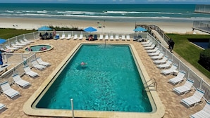 Un espace piscine avec vue sur la plage, des chaises longues et des parasols.