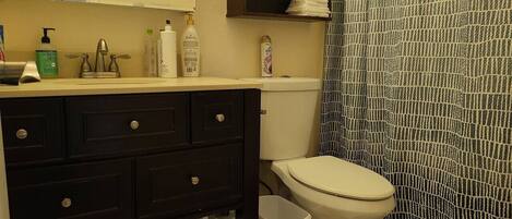 A bathroom with a toilet, a sink with toiletries, a dark-colored cabinet, and a patterned shower curtain.