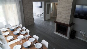 Un coin repas avec une table en bois dressée pour six personnes, des chaises blanches et une cheminée.