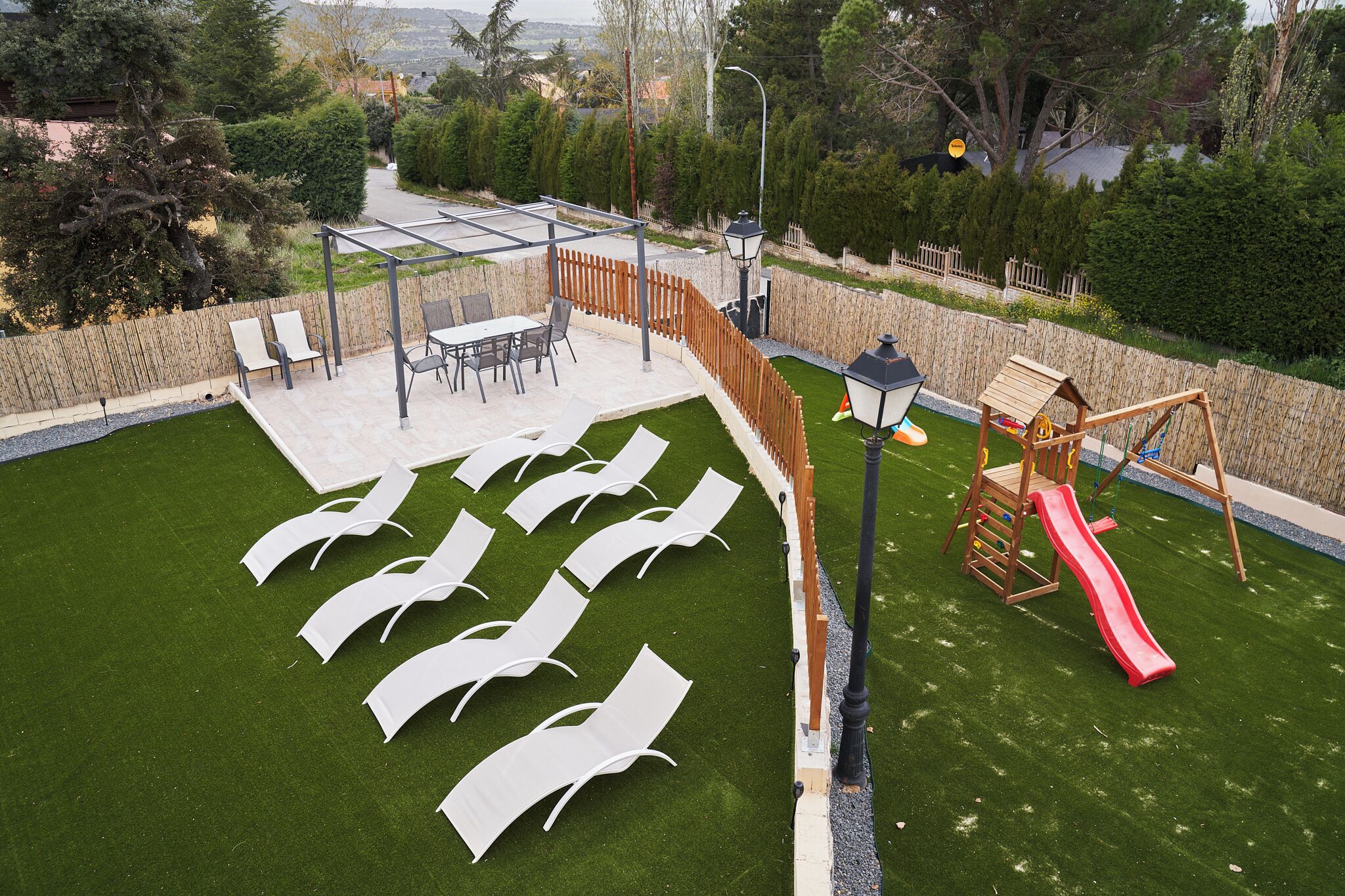 Un jardin avec une pelouse artificielle, une structure de jeu en bois et un espace détente avec des chaises et une table.