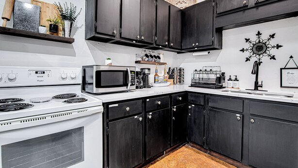 A kitchen with dark cabinets, a white stove, and a microwave. - Old Town Rodeo Studio. Free parking. Walk to entertainment and restaurants. (Burleson)