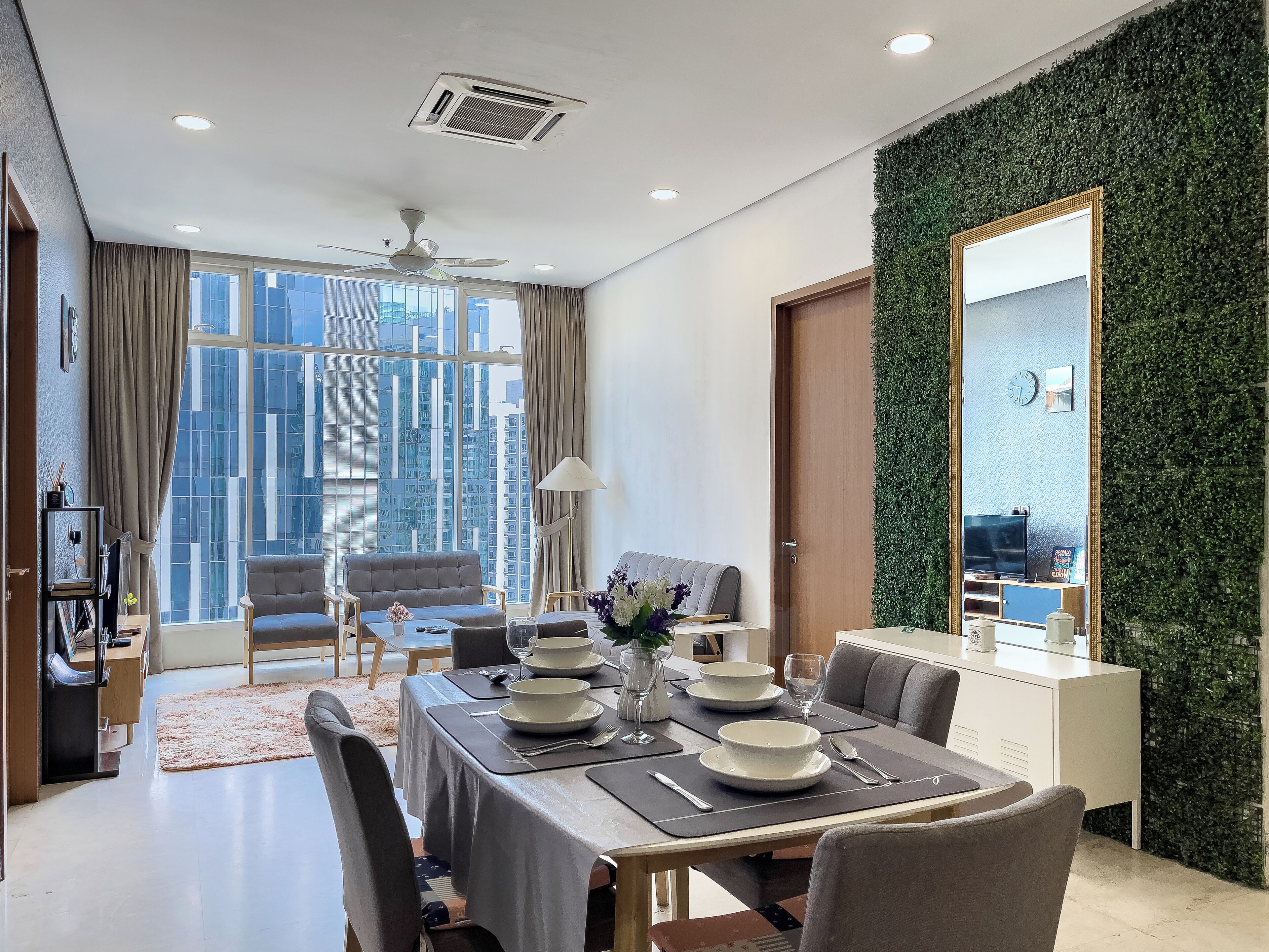 Un comedor moderno con una mesa dispuesta para cuatro, un sofá y vistas de edificios altos a través de amplias ventanas.